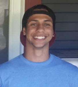 A happy young Black man wearing a baseball cap backwards is smiling into the camera
