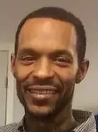 A Black man is facing the camera and smiling.